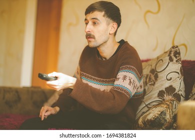 A Man Watches TV. A Man With A Remote Control In His Hands. Serious Man With A Remote Control In His Hands. Vintage Photo Processing.