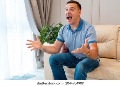 Man Watching Football In Living Room. Millenial Man At Home Alone Watching Soccer Games On Tv Enjoying And Celebrating Goal And Gestures Of Victory Sitting On Couch Happy And Excited