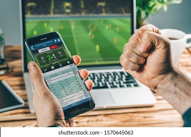 Man watching football play online broadcast on his laptop, cheering for his favourite team, making bets at bookmaker's website.