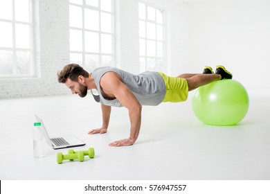 Man Watching Online Trainig With Laptop Training On The Fitball In The Gym