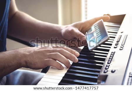 Man watching piano tutorial video with mobile phone. Person practising playing with an online lesson and course. Internet class to learn a new instrument. Pianist training with smartphone.