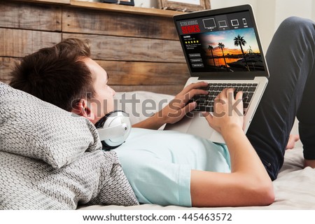Man watching streaming series in a laptop computer, lying in the bed at home.