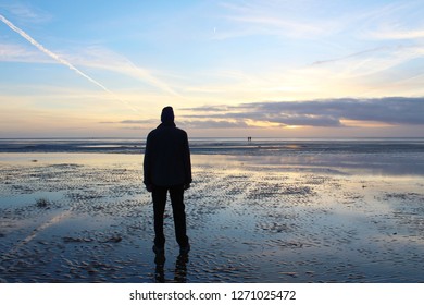 Man is watching the sunset on the mud flat of a North Sea beach, Island of Fanoe, Denmark