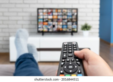 Man Watching TV, Lying On Sofa, Legs On Table. Person Holding Remote Control In Living Room