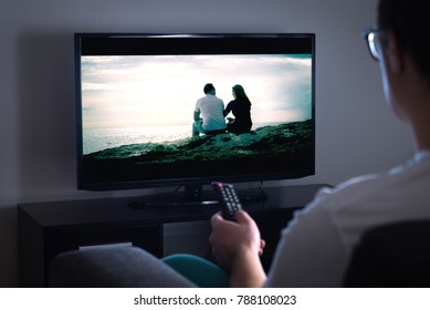 Man watching tv or streaming movie or series with smart tv at home. Film or show on television screen. Person holding the remote control or switching channel. Turning on or off tv.
