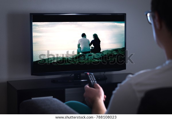 Man\
watching tv or streaming movie or series with smart tv at home.\
Film or show on television screen. Person holding the remote\
control or switching channel. Turning on or off\
tv.\
