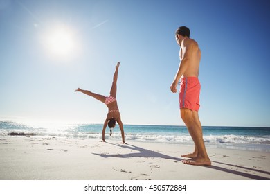 Man Watching Woman While Performing Somersault On Beach