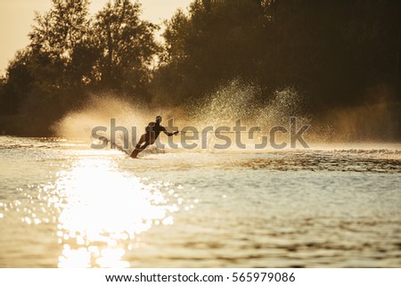 Man water skiing at sunset. Man riding wakeboard on lake water.