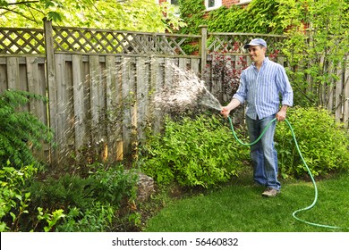 Man Watering The Garden With Hose In Backyard