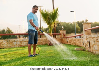 Man Watering The Lawn With A Hose In The Morning