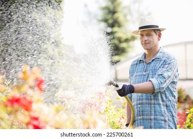 Man Watering Plants Outside Greenhouse