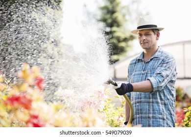 Man Watering Plants Outside Greenhouse