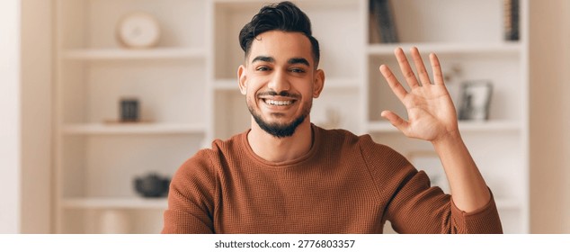 Man Waves Hello While Sitting in a Room With Shelves and Decor During Daytime