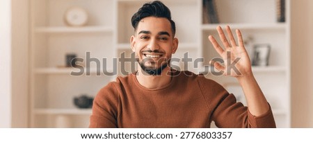 Man Waves Hello While Sitting in a Room With Shelves and Decor During Daytime