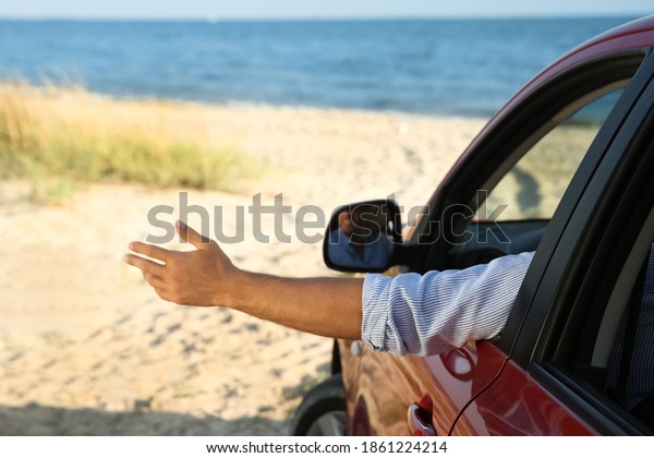 Man\
waving from car window on beach, closeup. Summer\
trip