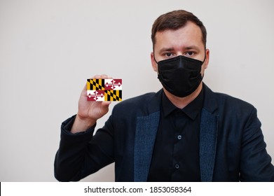 Man Wear Black Formal And Protect Face Mask, Hold Maryland Flag Card Isolated On White Background. USA Coronavirus Covid Country Concept.