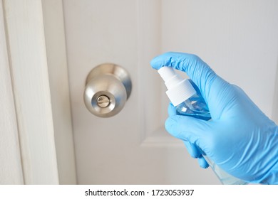 A Man Wear Blue Glove Disinfecting To The Doorknob With Alcohol Spray During The COVID-19 Pandemic. Spraying Alcohol To Clean The Doorknob Before Touched It.