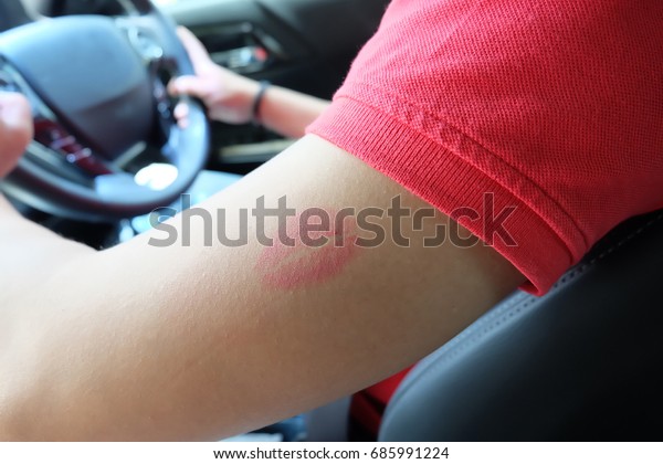 A man wear polo\
shirt is driving a car , his arm have pink kisses lip , couple in\
love and romantic concept