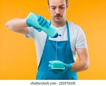 man wearing apron pouring liquid detergent on sponge, against yellow background - Shutterstock ID 255976105
