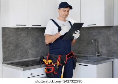 Man wearing a belt with various tools and using a tablet stands against background of a new kitchen - Powered by Shutterstock