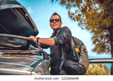 Man wearing black denim shirt and sunglasses opening cargo box on roof rack after hiking