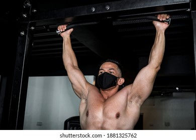 A Man Wearing A Black Face Mask Working Out At The Gym Doing Some Pullups. New Normal Scene At A Public Fitness Center.