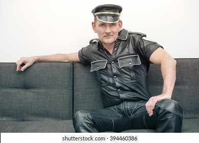 Man Wearing Black Fetish Leather Clothes And Sitting On Couch