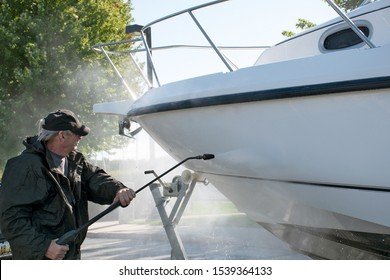 man wearing black waterproof suit while pressure washing boat hull