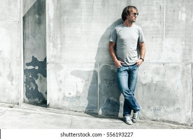 Man Wearing Blank T-shirt Posing Against Gray Concrete Wall In The City Street, Front Tshirt Mockup On Model, Urban Style