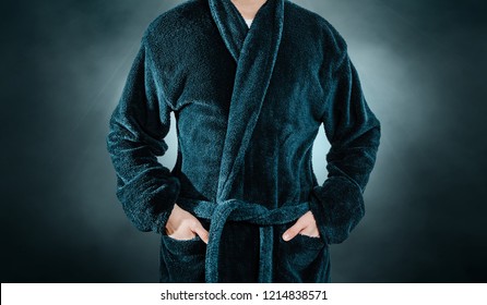 A Man Wearing A Blue Bathrobe, Bathrobes Is Holding His Hands In His Pocket. The Concept Of Rest, A Day Off Work. The Sick Man Spends His Day Off At Home, Resting In Front Of The TV.