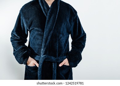 A Man Wearing A Blue Bathrobe, Bathrobes Is Holding His Hands In His Pocket. The Concept Of Rest, A Day Off Work. The Sick Man Spends His Day Off At Home, Resting In Front Of The TV.