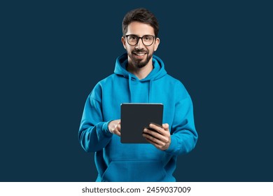 A man wearing a blue hoodie is holding a tablet device in his hands. The man appears focused while interacting with the screen of the tablet. - Powered by Shutterstock