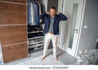 Man wearing a blue jacket while standing in front of his closet. Getting dressed and preparing for the day.