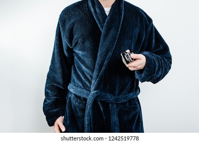 A Man Wearing A Blue Robe, Bathrobes Is Holding A TV Remote Control. The Concept Of Rest, A Day Off Work. The Sick Man Spends His Day Off At Home, Resting In Front Of The TV.