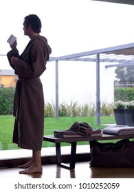 Man Wearing A Brown Bathrobe Having A Coffee Mug Looking Outside The Window