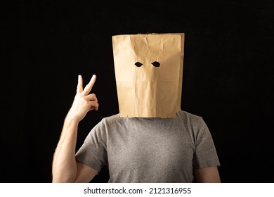 Man Wearing A Brown Paper Bag Over His Head And Holding Up Two Fingers.