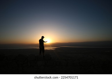 Man wearing a cap reaching hand out to touch the sun. Sunrise. - Shutterstock ID 2254701171