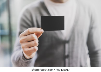 Man wearing casual shirt and showing blank black business card. Blurred background. Horizontal mockup