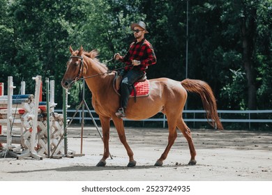 Man wearing a cowboy hat and plaid shirt riding a brown horse at an outdoor equestrian facility surrounded by greenery and jumps. - Powered by Shutterstock