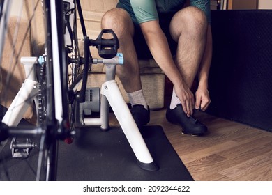 Man Is Wearing A Cycling Shoes To Get Training On The Bike With A Smart Trainer At Home. Stay Fit And Active While At Home. Indoor Cycling In Winter.