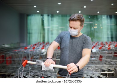 Der Mensch mit einer Einweg-medizinischen Gesichtsmaske wischt den Warenkorb mit einem Desinfektionstuch im Supermarkt ab. Sicherheit während des Ausbruchs von Coronavirus. Epidemie des Virus covid.