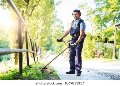 Man Wearing Ear Protectors Mowing Grass In The Backyard With Petrol Hedge Trimmer