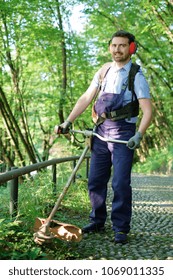 Man Wearing Ear Protectors Mowing Grass In The Backyard With Petrol Hedge Trimmer