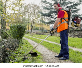 Man Wearing  Ear Protectors Mowing Grass In The Backyard With Petrol Hedge Trimmer