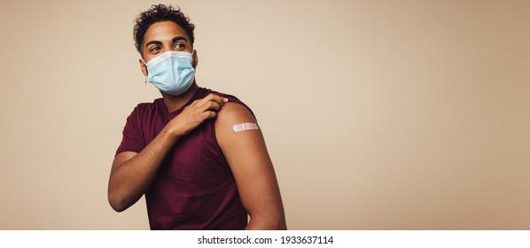 Homem usando máscara facial mostrando o braço vacinado. Homem com máscara protetora recebeu uma vacina corona desviando o olhar sobre fundo marrom.