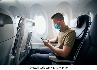 Man wearing face mask and using phone inside airplane during flight. Themes new normal, coronavirus and personal protection.  - Powered by Shutterstock