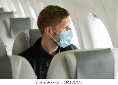 A Man Wearing Face Mask While Sitting Into An Airplane. New Normal Traveling During A Pandemic. Male Passenger Traveling By Plane. Wearing Mask In Aircraft Cabin. Air Travel Covid 19