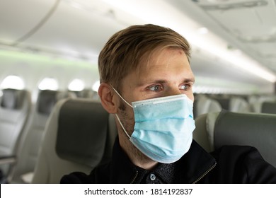 A Man Wearing Face Mask While Sitting Into An Airplane. New Normal Traveling During A Pandemic. Male Passenger Traveling By Plane. Wearing Mask In Aircraft Cabin. Air Travel Covid 19