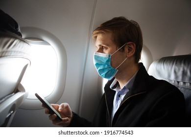 A Man Wearing Face Mask While Sitting Into An Airplane. New Normal Traveling During A Pandemic. Male Passenger Traveling By Plane. Wearing Mask In Aircraft Cabin. Air Travel Covid 19