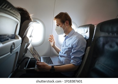 A Man Wearing Face Mask While Sitting Into An Airplane. New Normal Traveling During A Pandemic. Male Passenger Traveling. Wearing FFP2 Mask In Aircraft Cabin. Travel Covid-19 Work From Plane On Laptop